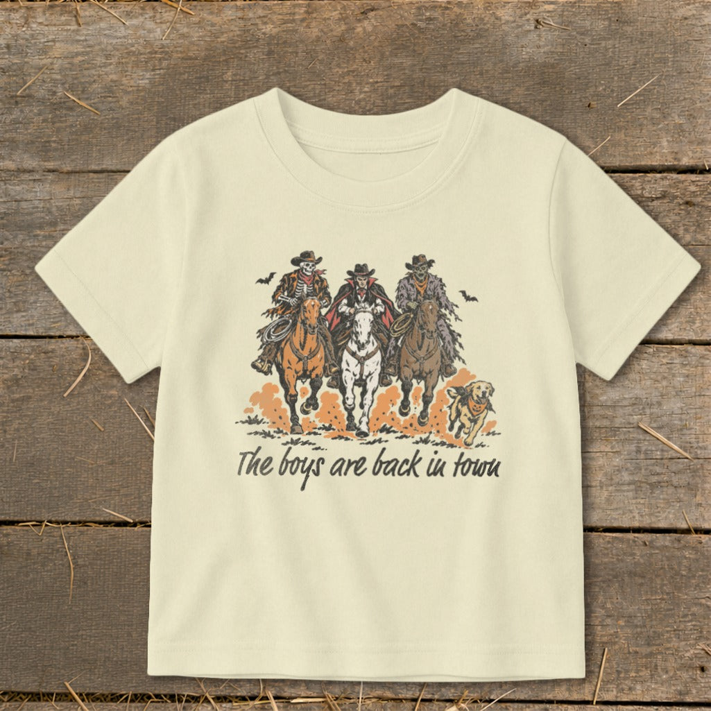 Three skeleton cowboys and a vampire ride horses with a dog, text reads "The boys are back in town".