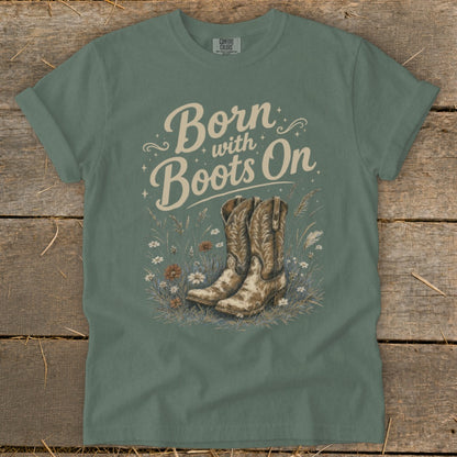 Green t-shirt with "Born with Boots On" text and cowboy boots in grass.