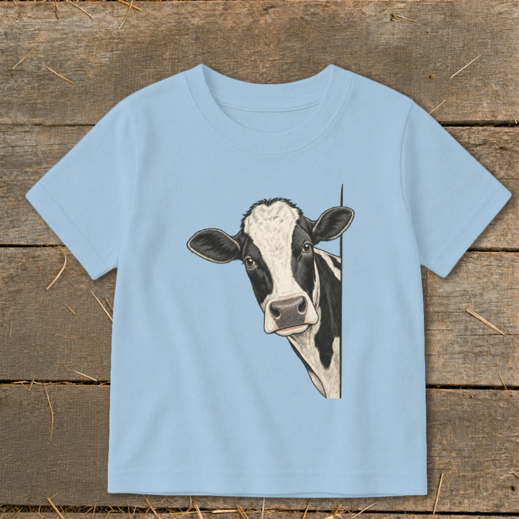 Black and white cow peeking from behind a white line on a light blue t-shirt.