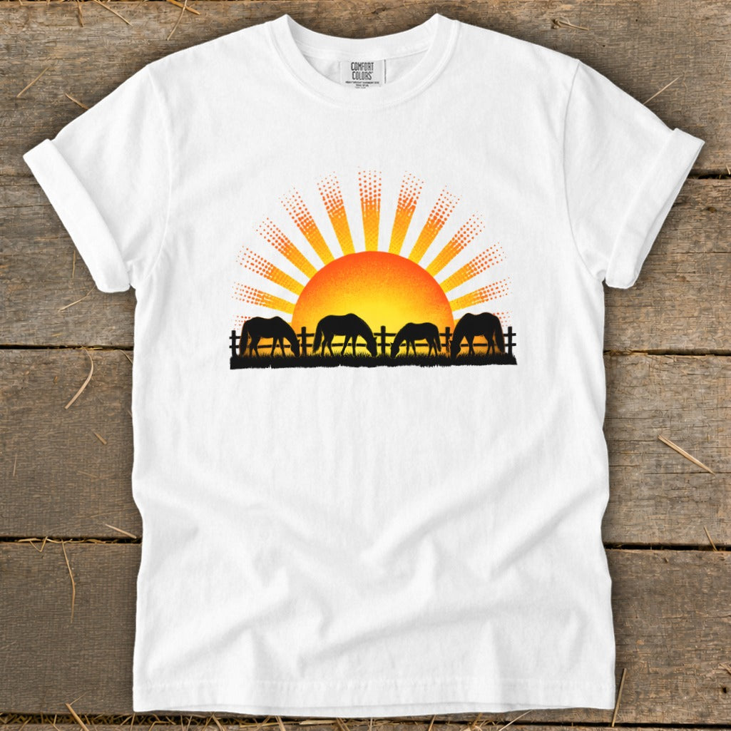 Silhouetted horses graze by a fence under a dotted sunrise on a white t-shirt.