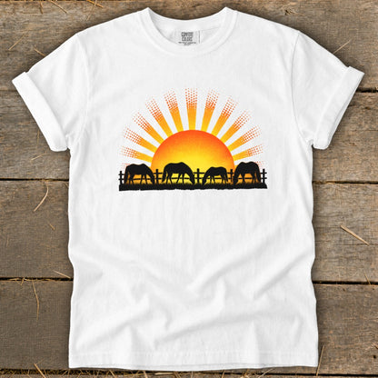 Silhouetted horses graze by a fence under a dotted sunrise on a white t-shirt.