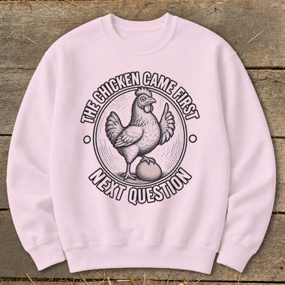 Light pink sweatshirt with graphic of chicken standing on egg, text "The chicken came first next question".