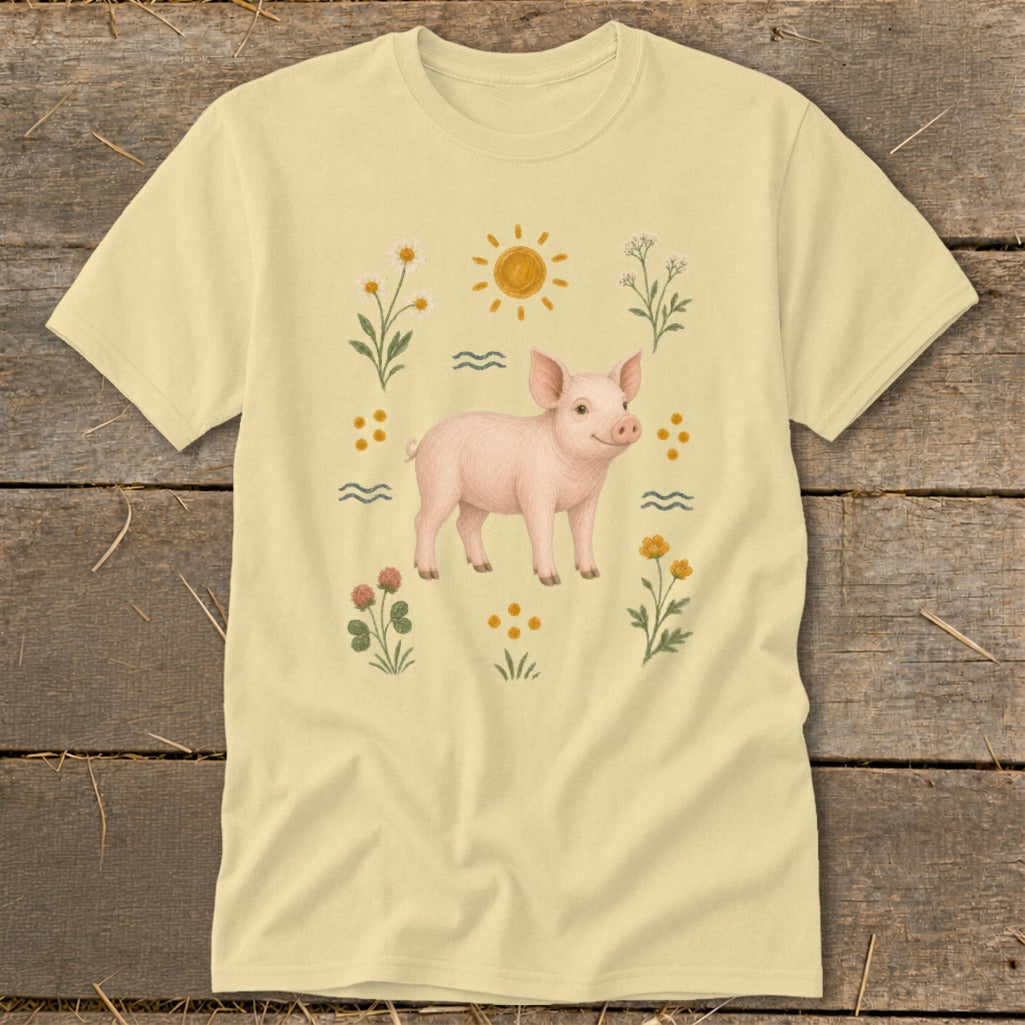 Light yellow t-shirt with a watercolor illustration of a pink pig surrounded by flowers and sun.