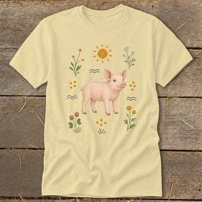 Light yellow t-shirt with a watercolor illustration of a pink pig surrounded by flowers and sun.