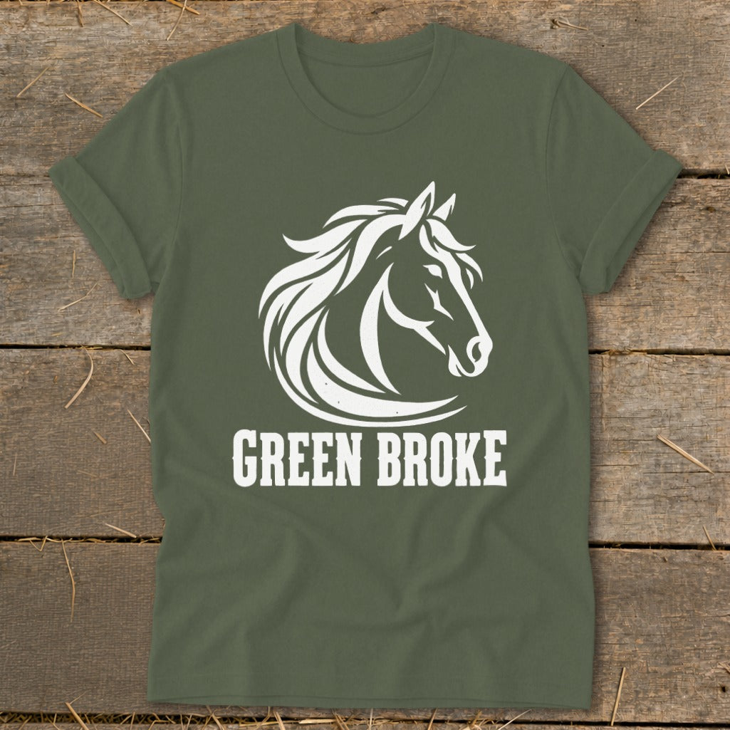 Olive green t-shirt with a white horse head graphic and the text GREEN BROKE on a wooden background.
