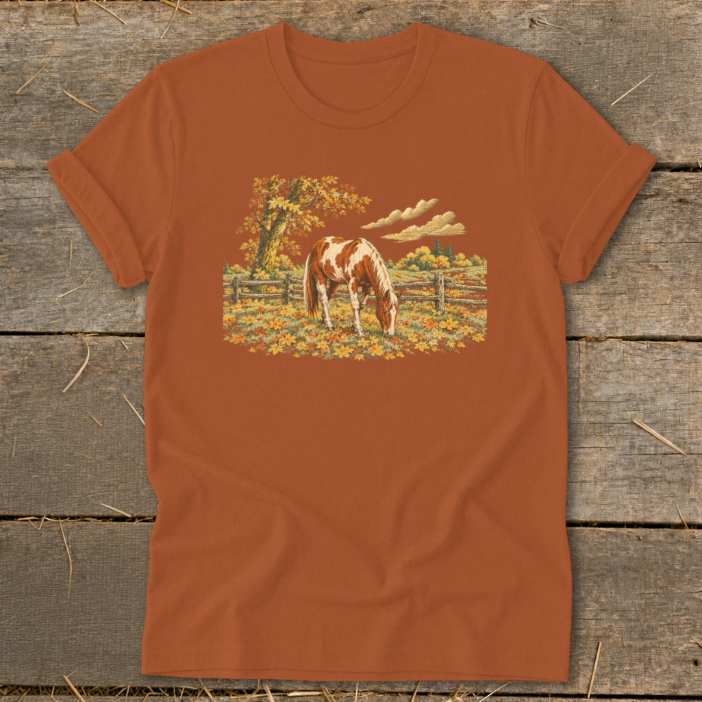 Brown and white horse grazing in autumn field with wooden fence and colorful trees.