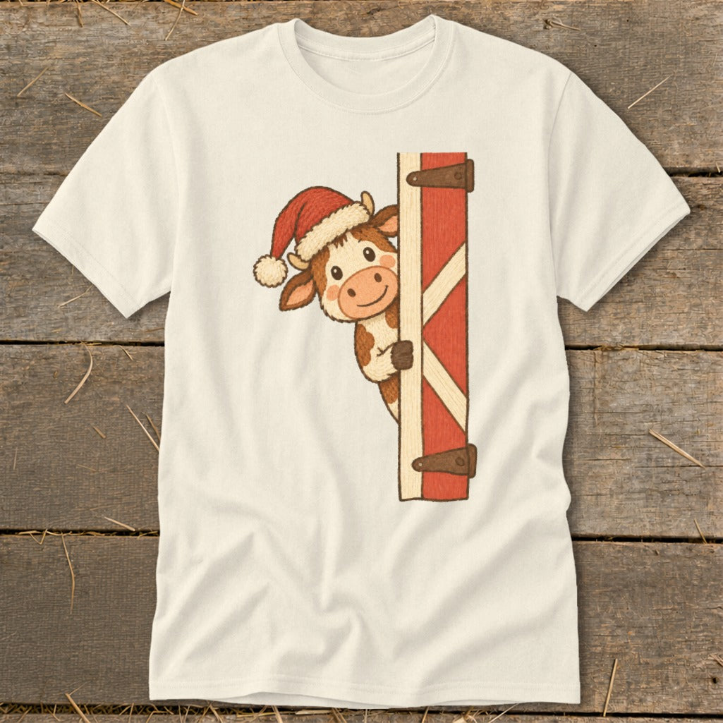 Cream t-shirt with a cartoon cow wearing a Santa hat peeking around a barn door.