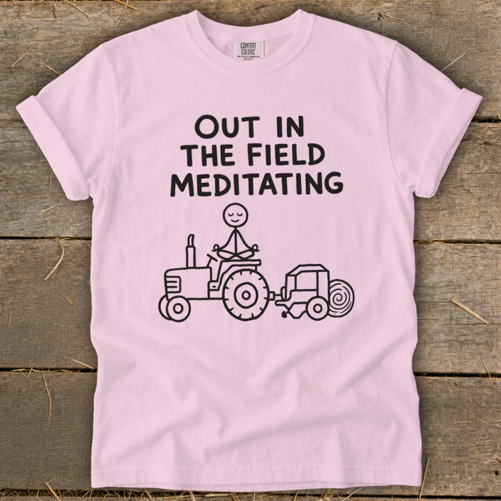 Pink t-shirt with "Out in the Field Meditating" text and stick figure meditating on tractor.