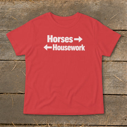 A red t-shirt with white text reading Horses and Housework, laid flat on a wooden background.