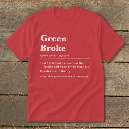 A red t-shirt lies flat on a rustic wooden surface, featuring dictionary-style text defining Green Broke.