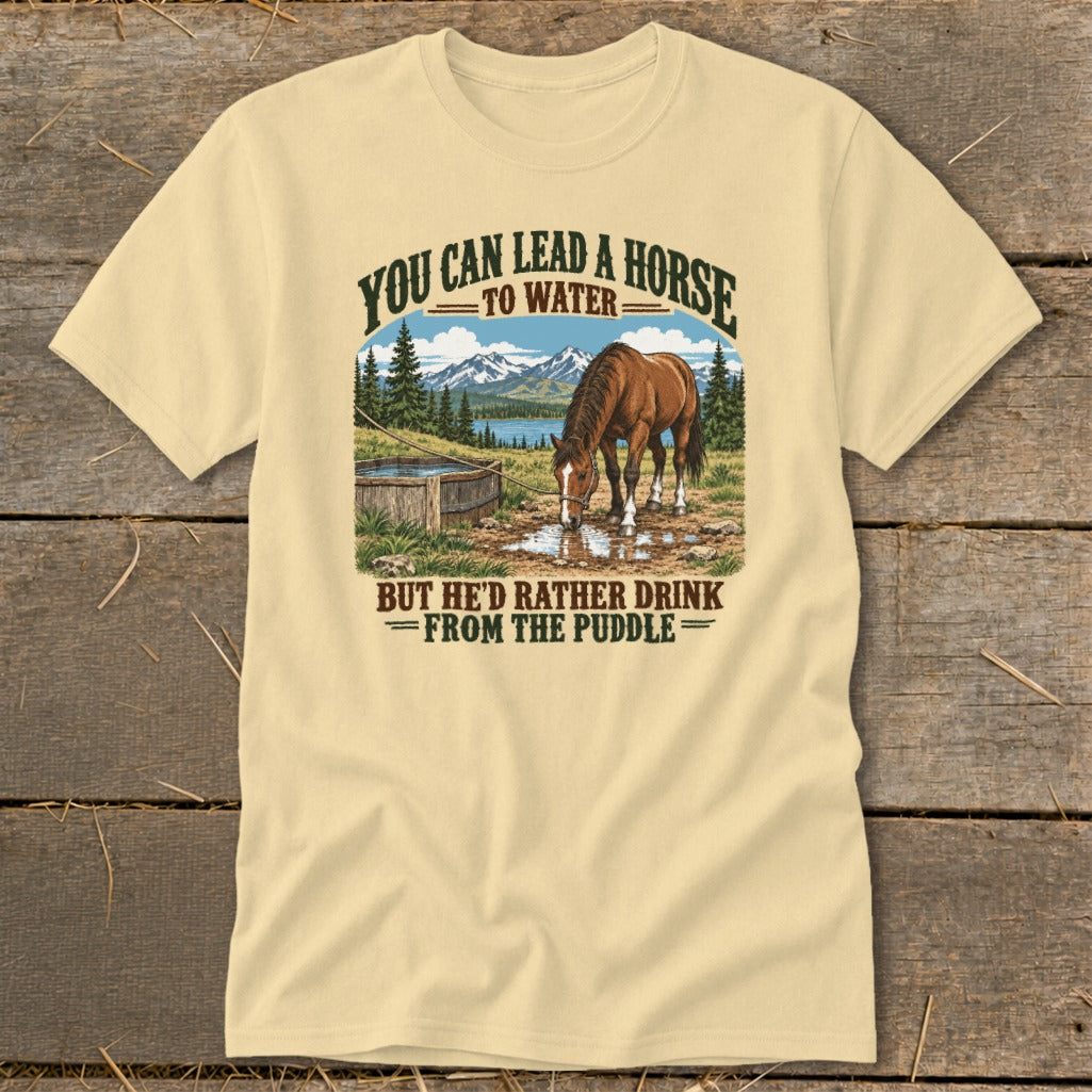 A light yellow t-shirt featuring a graphic of a horse drinking from a puddle with humorous text.