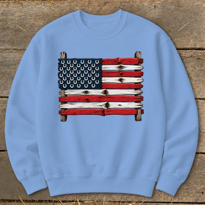 Light blue crewneck sweatshirt featuring a graphic of an American flag made from weathered wooden planks and horseshoes.