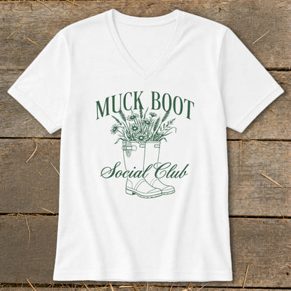 White t-shirt with green text "MUCK BOOT Social Club" and illustration of boots with flowers.