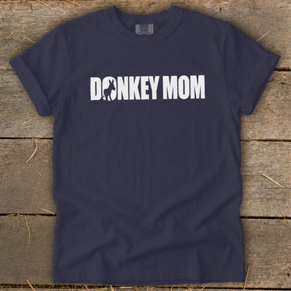 Navy blue short-sleeve t-shirt with white text reading DONKEY MOM and a donkey silhouette inside the letter O, laid flat on a rustic wooden surface.