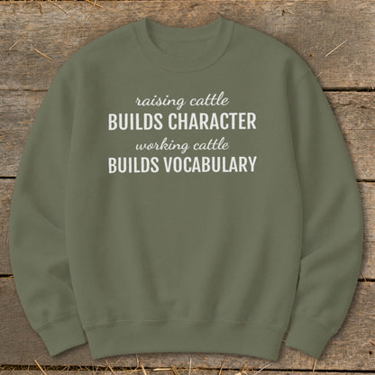 Olive green sweatshirt with white text that reads "raising cattle BUILDS CHARACTER, working cattle BUILDS VOCABULARY".