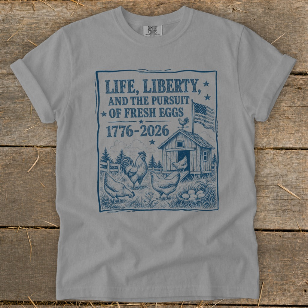 "Life, Liberty, and the Pursuit of Fresh Eggs 1776-2026" text on a grey t-shirt.