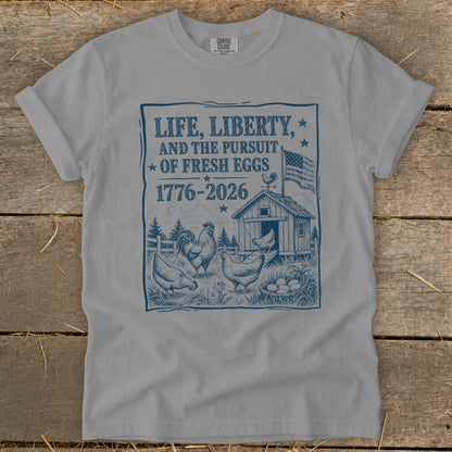 "Life, Liberty, and the Pursuit of Fresh Eggs 1776-2026" text on a grey t-shirt.