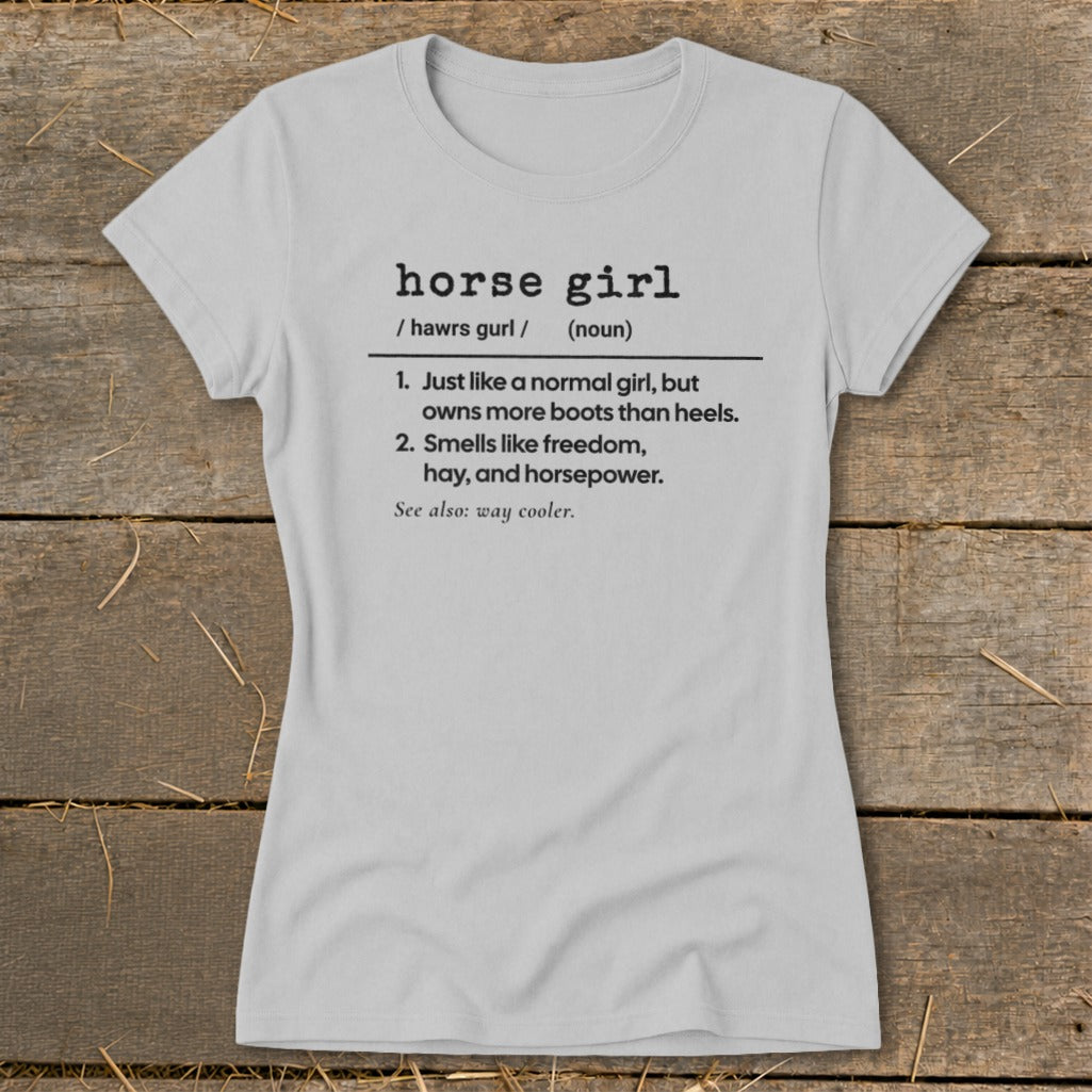 Light grey t-shirt with black text defining "horse girl" as someone who owns more boots than heels and smells like freedom.