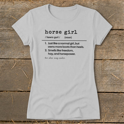 Light grey t-shirt with black text defining "horse girl" as someone who owns more boots than heels and smells like freedom.