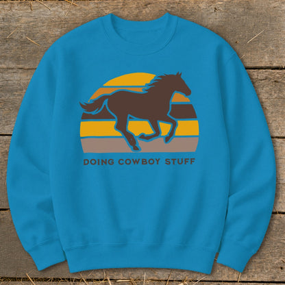 Teal sweatshirt with a brown horse silhouette over a striped sunset and "DOING COWBOY STUFF" text.