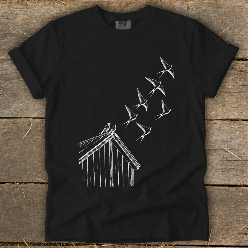 Black crewneck t-shirt featuring a white line drawing of a barn with birds flying upward.