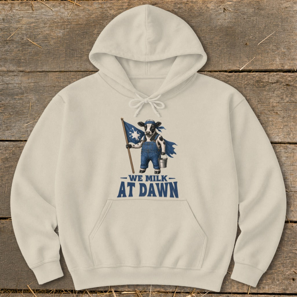Beige hoodie with a graphic of a cow holding a flag and text that reads "We Milk At Dawn."