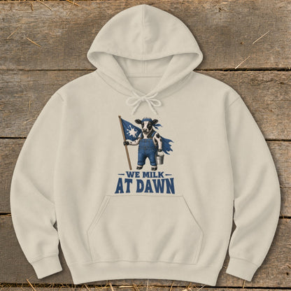 Beige hoodie with a graphic of a cow holding a flag and text that reads "We Milk At Dawn."
