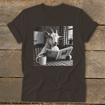 A dark brown t-shirt featuring a graphic of a goat sitting at a table reading a newspaper beside a coffee mug.