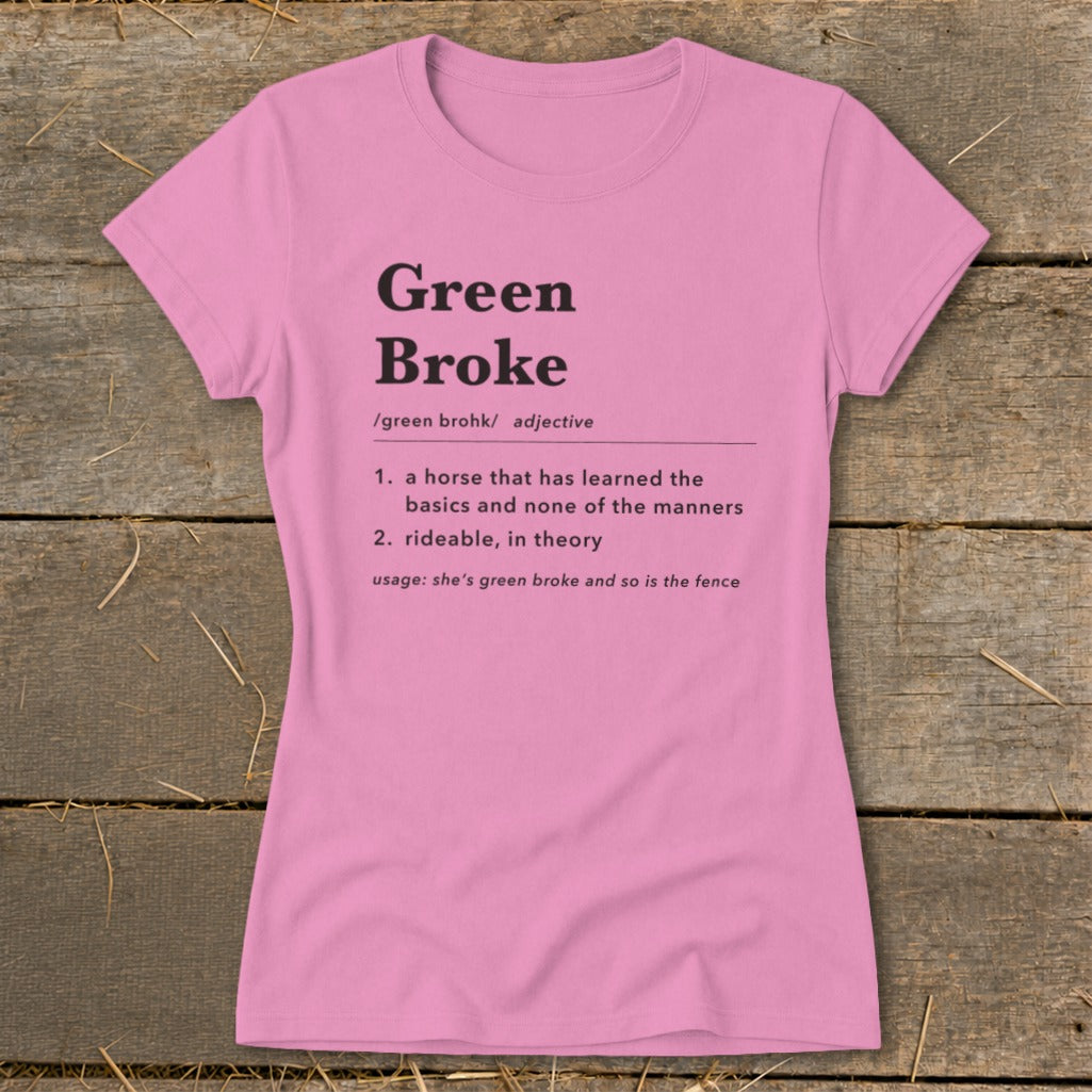 A pink women's t-shirt printed with a dictionary definition of Green Broke lies flat on a wooden surface.