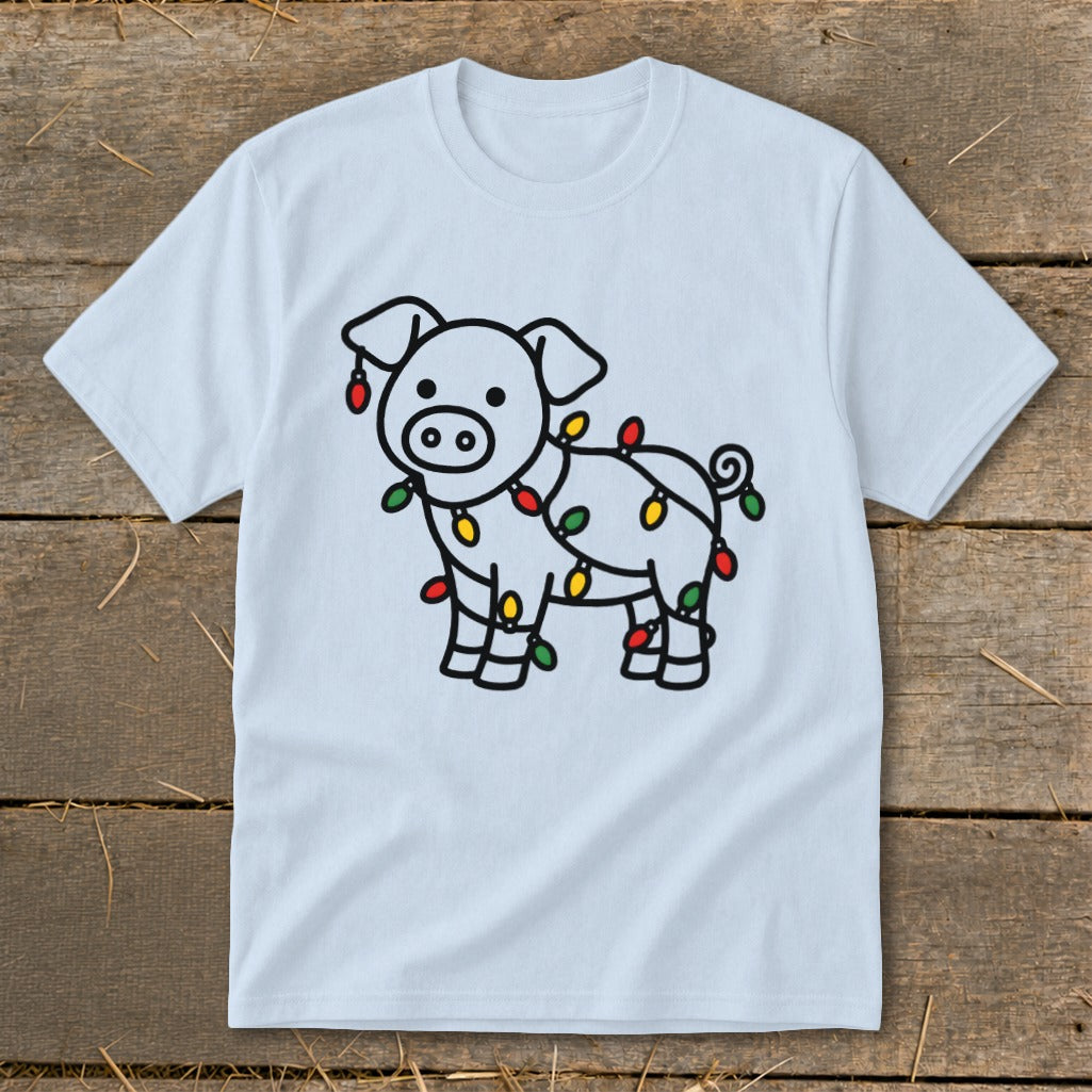 Light blue t-shirt featuring a cartoon pig wrapped in colorful Christmas lights, laid flat on wooden planks.
