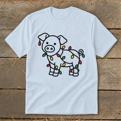 Light blue t-shirt featuring a cartoon pig wrapped in colorful Christmas lights, laid flat on wooden planks.