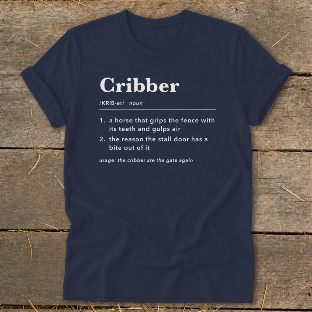 Navy blue t-shirt featuring dictionary-style text defining the word Cribber on a wooden surface.
