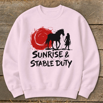 Pink sweatshirt with silhouette of horse and rider under a red sun, text "Sunrise & Stable Duty."