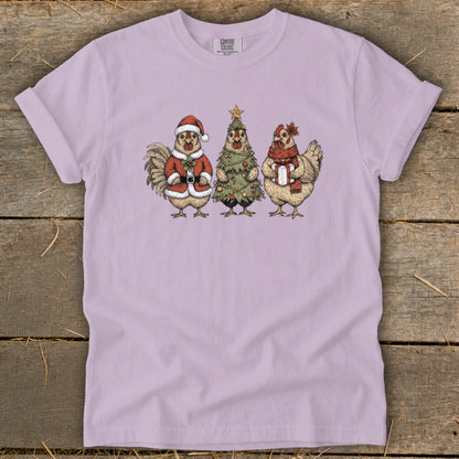 Rooster in Santa suit, chicken Christmas tree, and chicken with gift on light purple shirt.