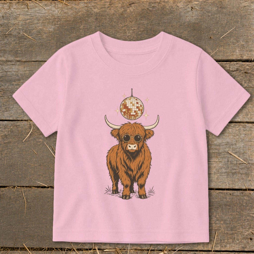 Pink t-shirt with a cartoon Highland cow wearing sunglasses under a disco ball.