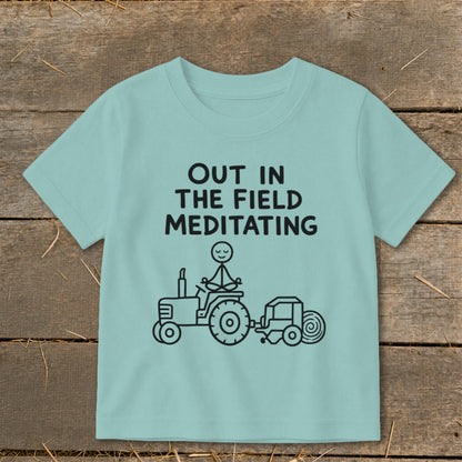 Light blue t-shirt with "OUT IN THE FIELD MEDITATING" and stick figure meditating on a tractor.