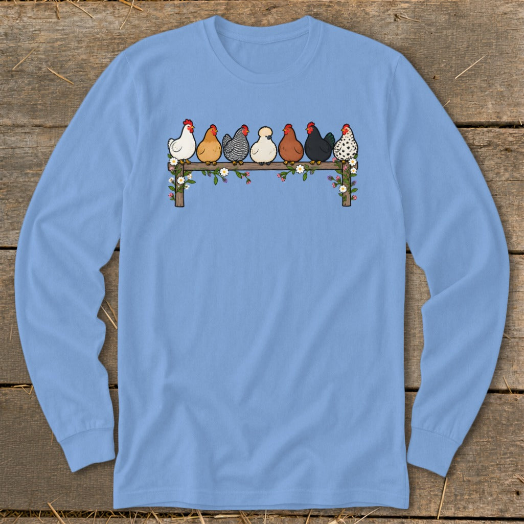 Light blue long-sleeved shirt with a graphic of seven colorful chickens sitting on a flower-adorned fence.