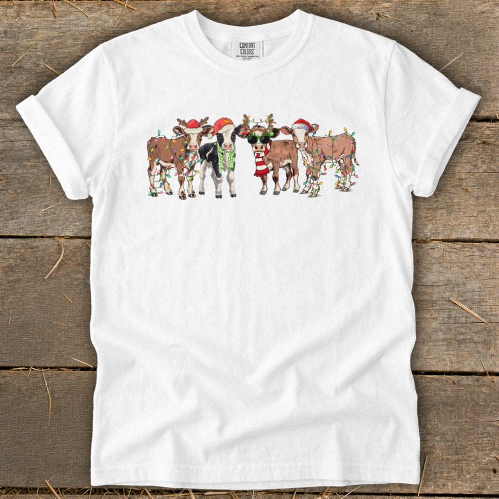 Five cartoon cows wear Santa hats and Christmas lights on a white t-shirt.