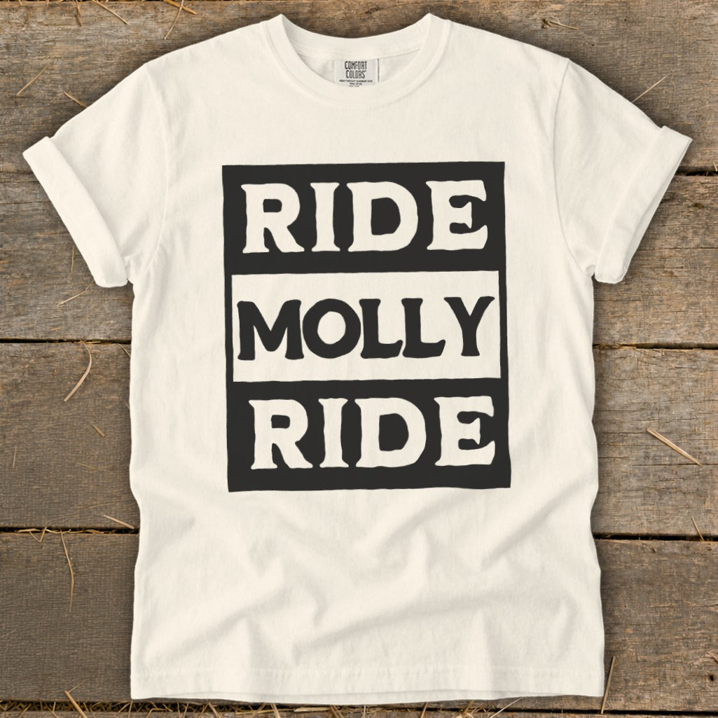 A cream-colored t-shirt on a wooden surface with the text "RIDE MOLLY RIDE" in bold, block letters.