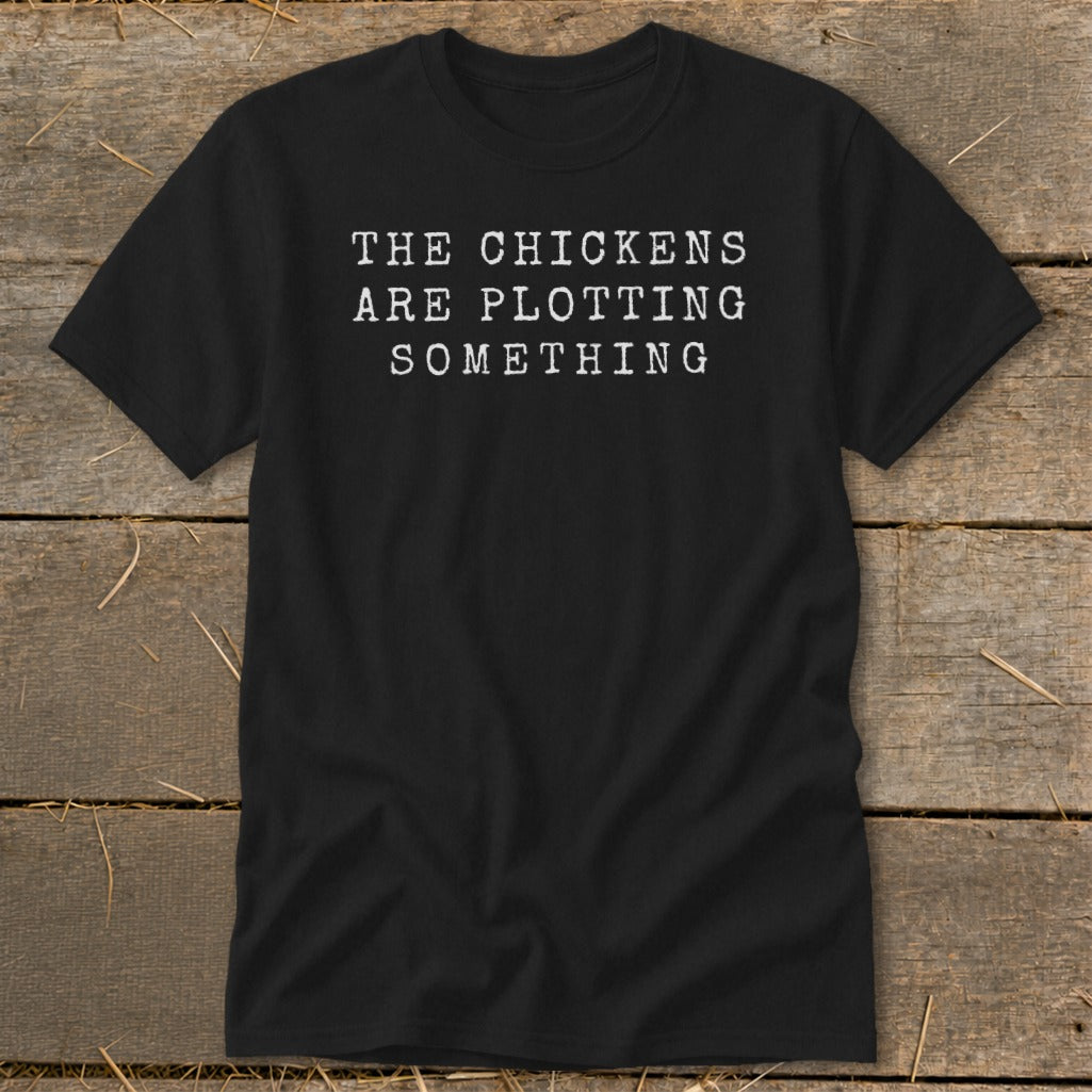 Black t-shirt with white text reading "THE CHICKENS ARE PLOTTING SOMETHING".