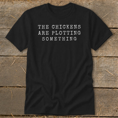 Black t-shirt with white text reading "THE CHICKENS ARE PLOTTING SOMETHING".