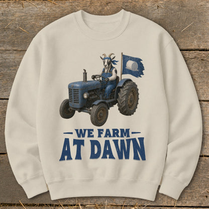 Cream sweatshirt with a goat driving a blue tractor, flying a flag. Text says "WE FARM AT DAWN".