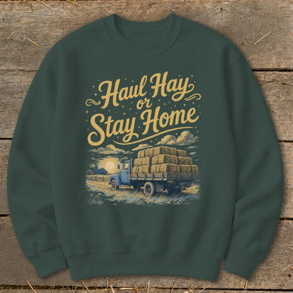 Green sweatshirt with "Haul Hay or Stay Home" text and illustration of a blue truck loaded with hay bales.