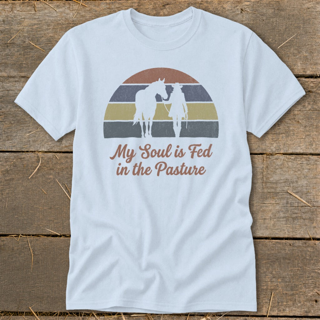 White t-shirt with retro graphic of horse and rider with text "My Soul is Fed in the Pasture".