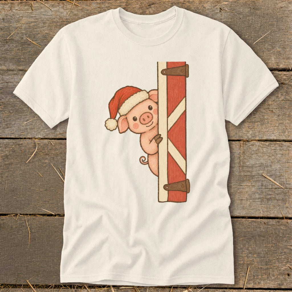 Pig wearing Santa hat peeks from behind a red barn door on a light shirt.