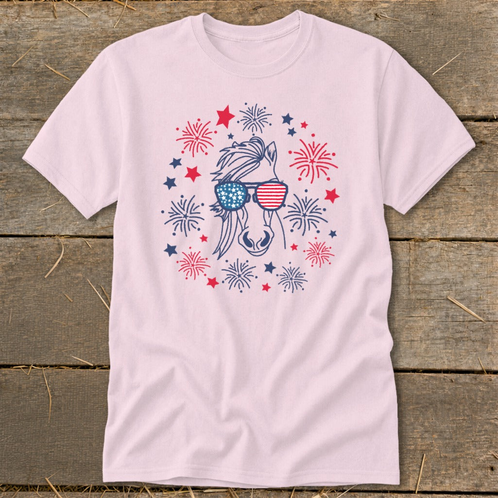 Horse head with American flag sunglasses surrounded by fireworks and stars graphic on pink t-shirt.