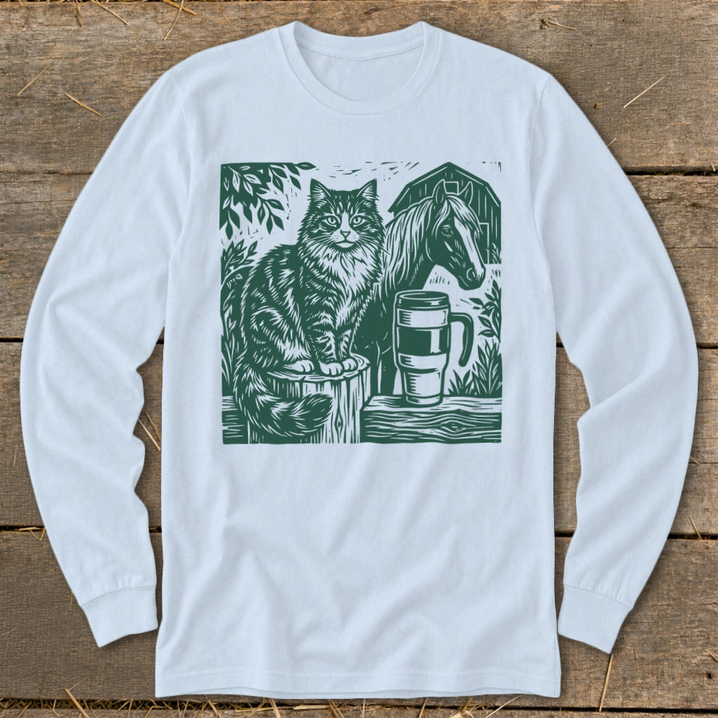Green linocut art of a cat, horse, mug, and barn on a white long-sleeved shirt.