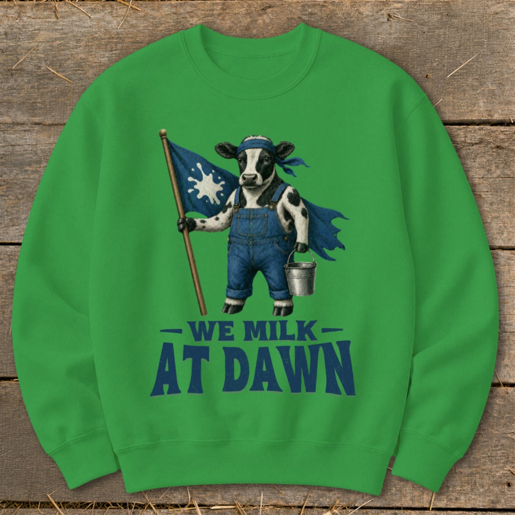 Green sweatshirt with cartoon cow in overalls holding flag and bucket, text "WE MILK AT DAWN".