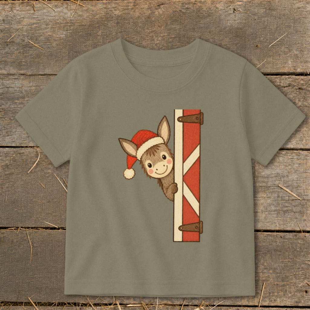 Donkey wearing Santa hat peeking from barn door on a taupe t-shirt.