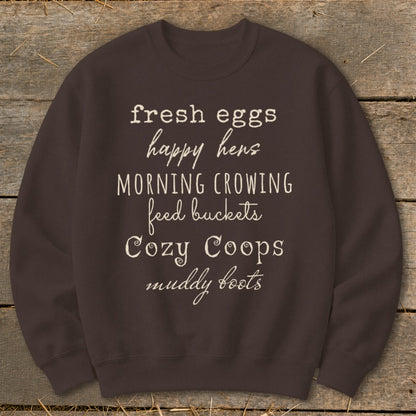 Brown sweatshirt with list of phrases: fresh eggs, happy hens, morning crowing, feed buckets, Cozy Coops, muddy boots.